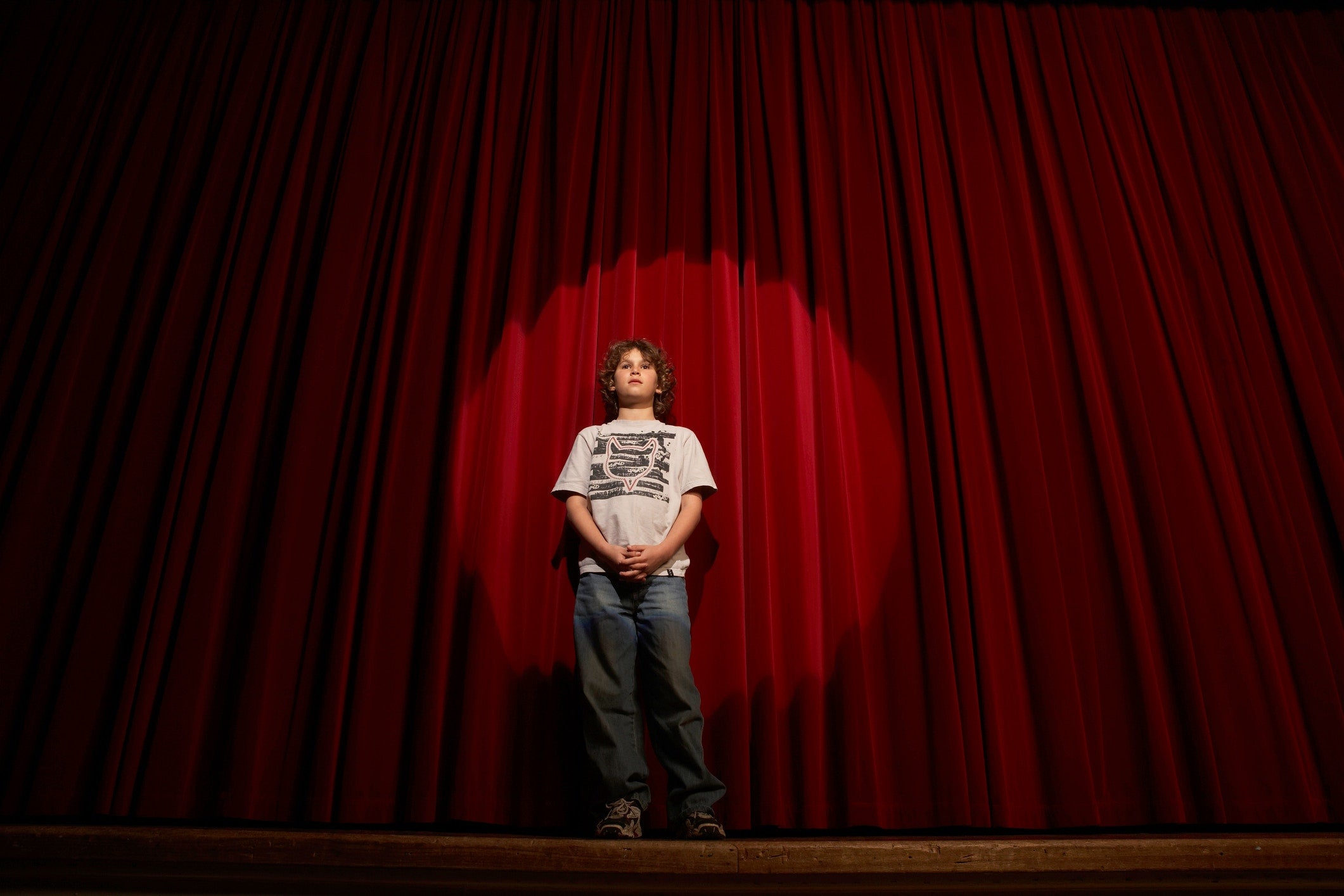 young boy performing at the stage with red curtains