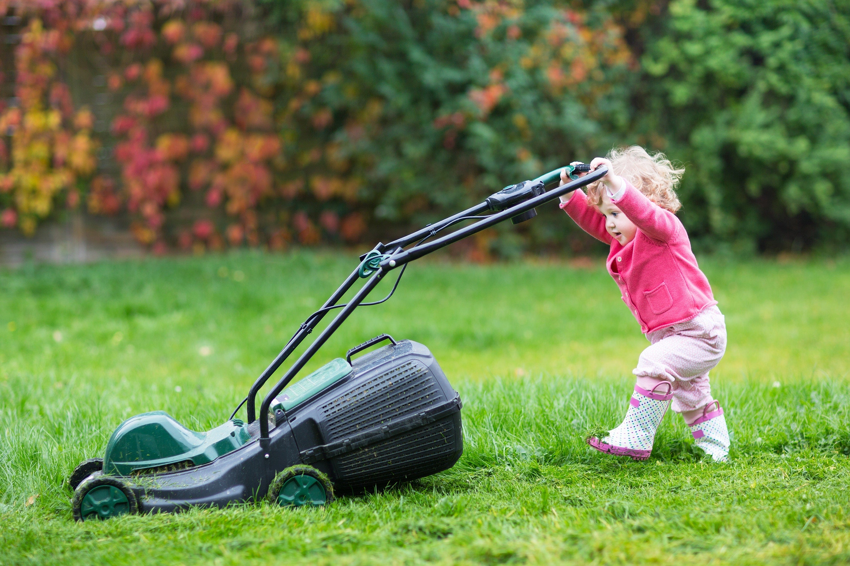 Cute curly baby girl with big green lawn mower