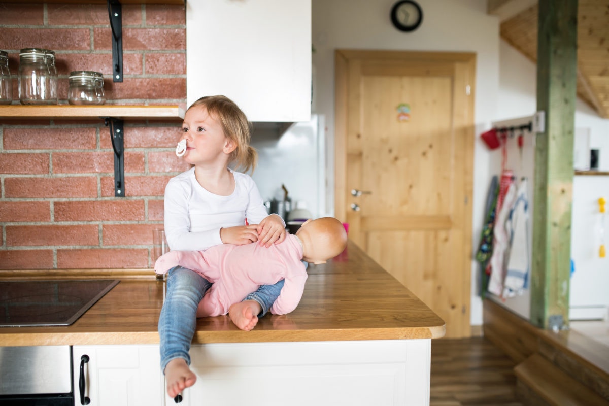 child holding a plastic baby siting on a table in a kitchen