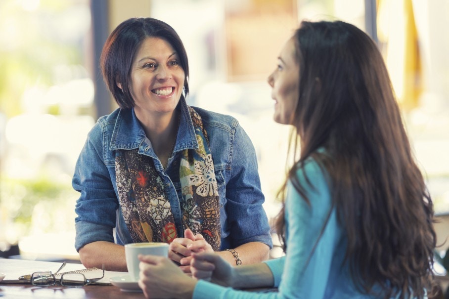 two women sitting at table and drinking cofee and smiling