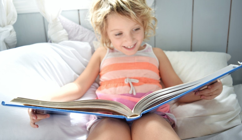 little girl reading book in bed