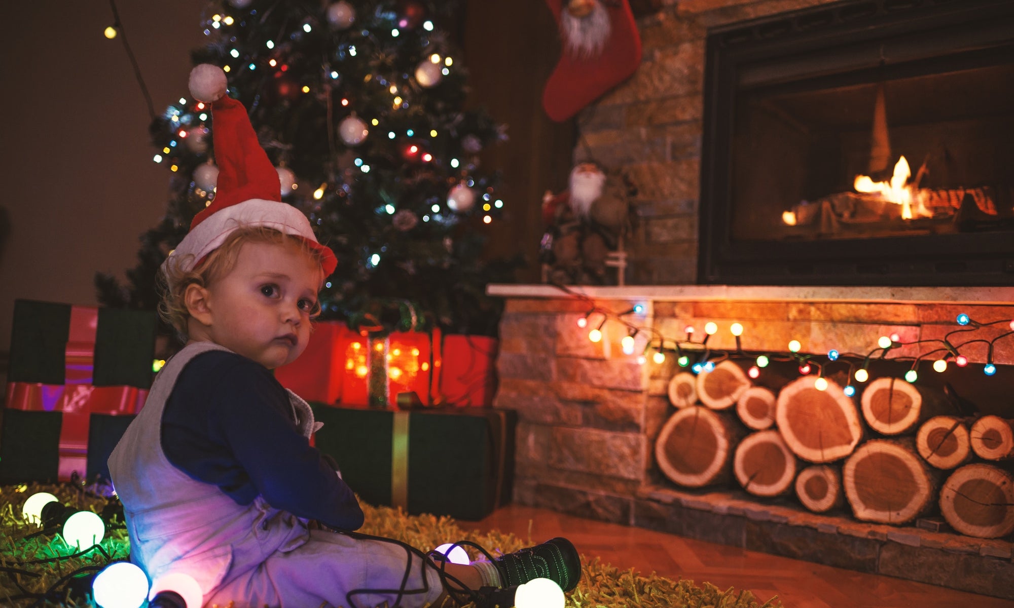 little baby boy in a Christmas cap sitting on floor by the Christmas tree