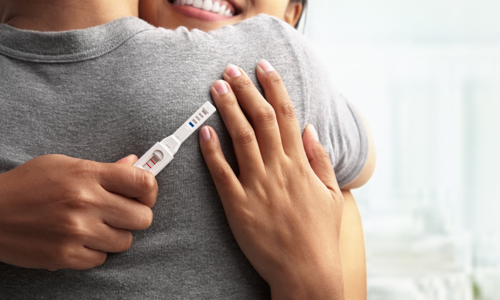 Young happy women hugging husband holding positive result pregnancy test