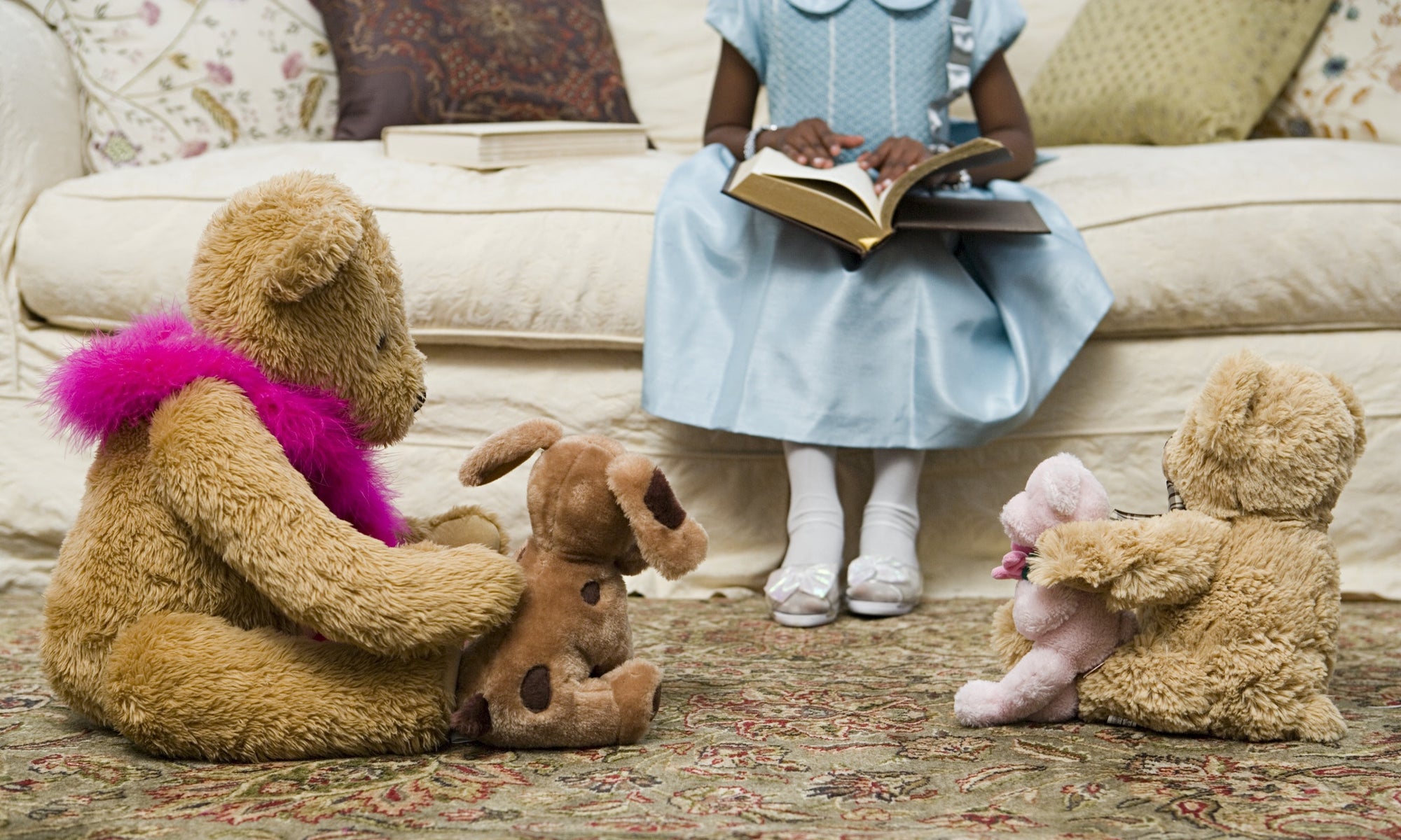 young girl sitting on sofa with book and teddy bear on floor