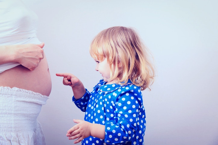 The little girl points a finger at a stomach of mother.