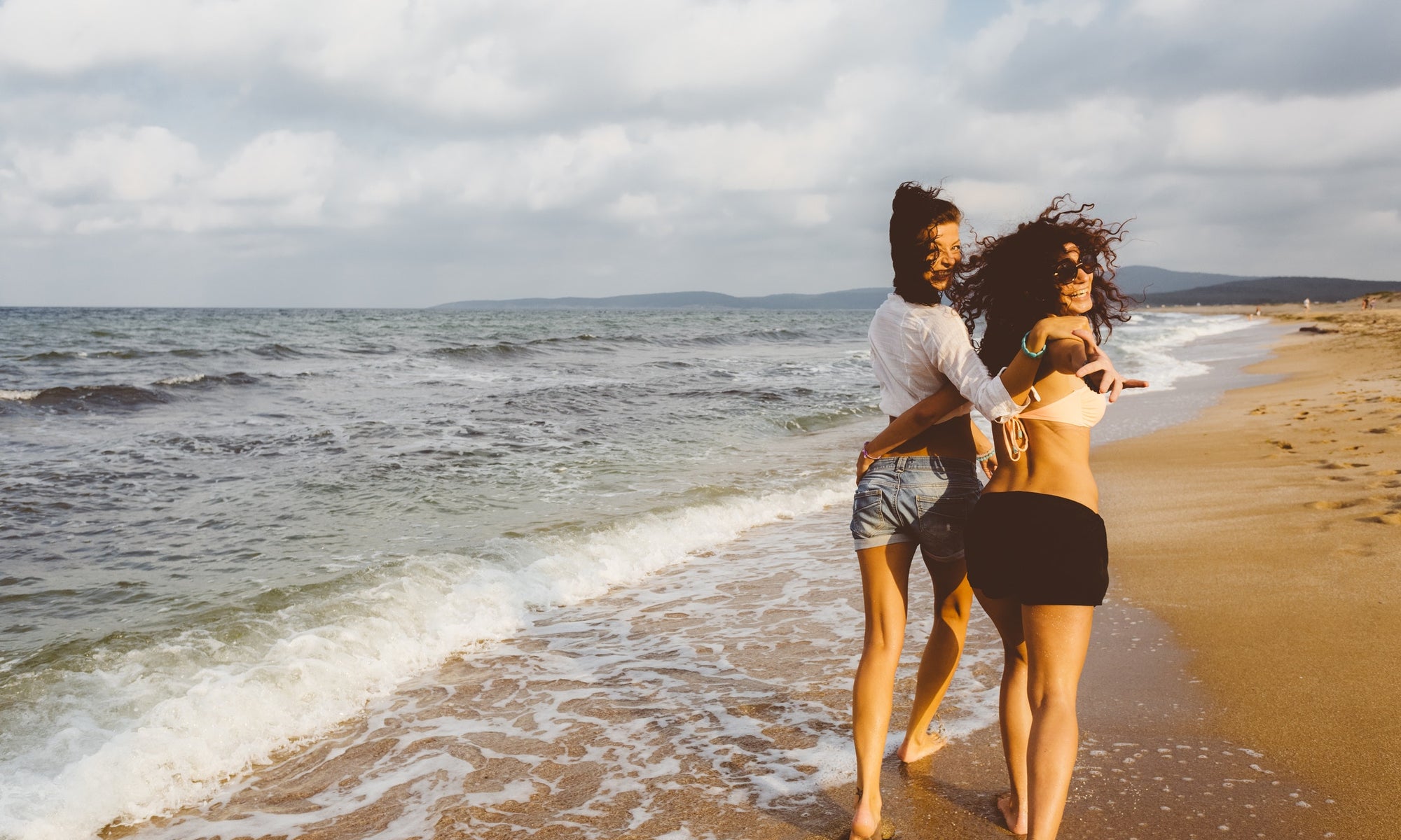 two beautiful women walking on the beach and smiling