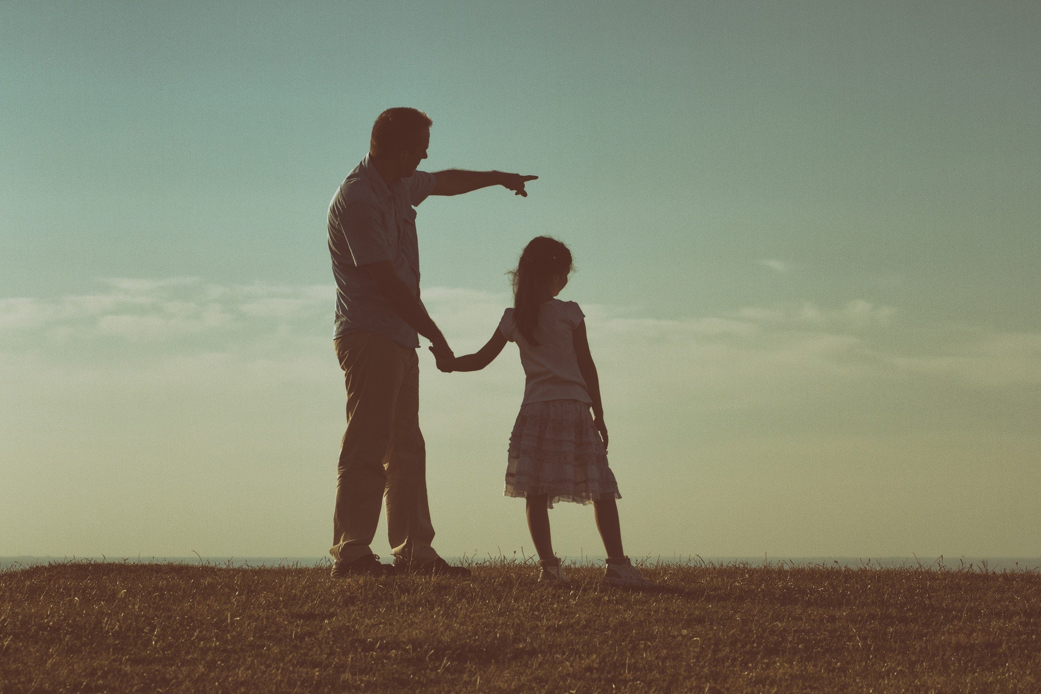 Father and daughter holding hands standing on a hill with nature lanscape back view.