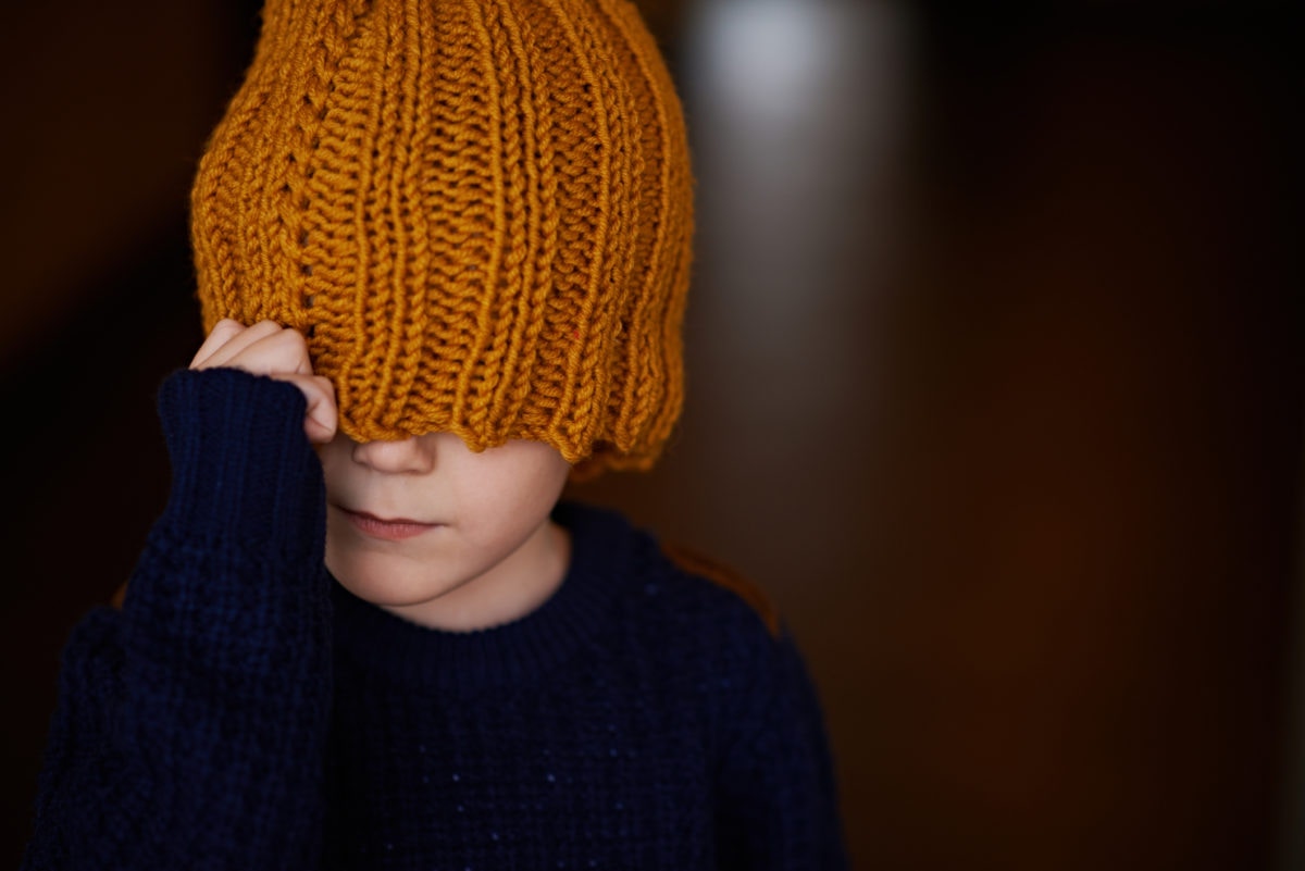 A boy is clsoing his eyes with wollen cap