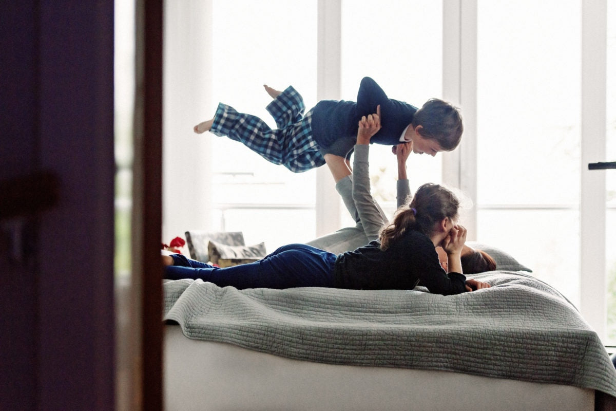 A mother is lifting his son on her legs while daugther watching