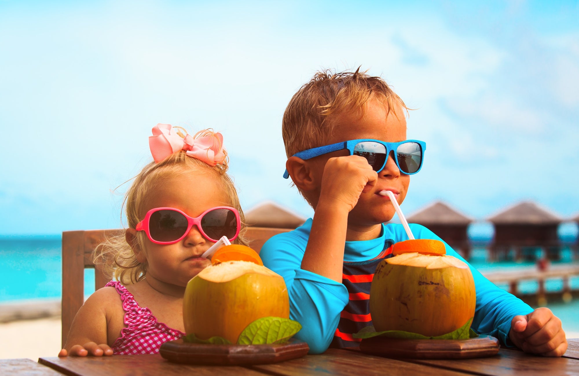 Two children on a table at beach side, wearing googles, drinking coconut water