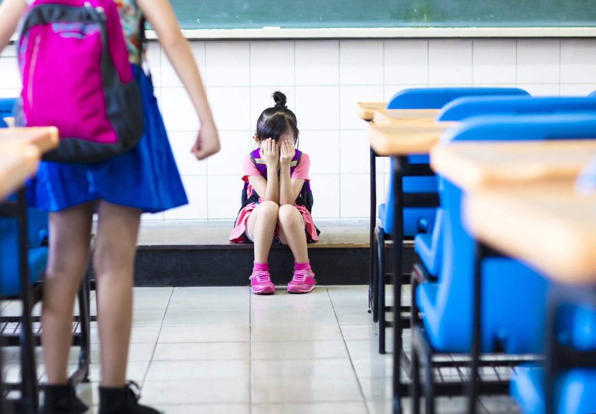 Une fille pleure dans une salle de classe en fermant son visage.