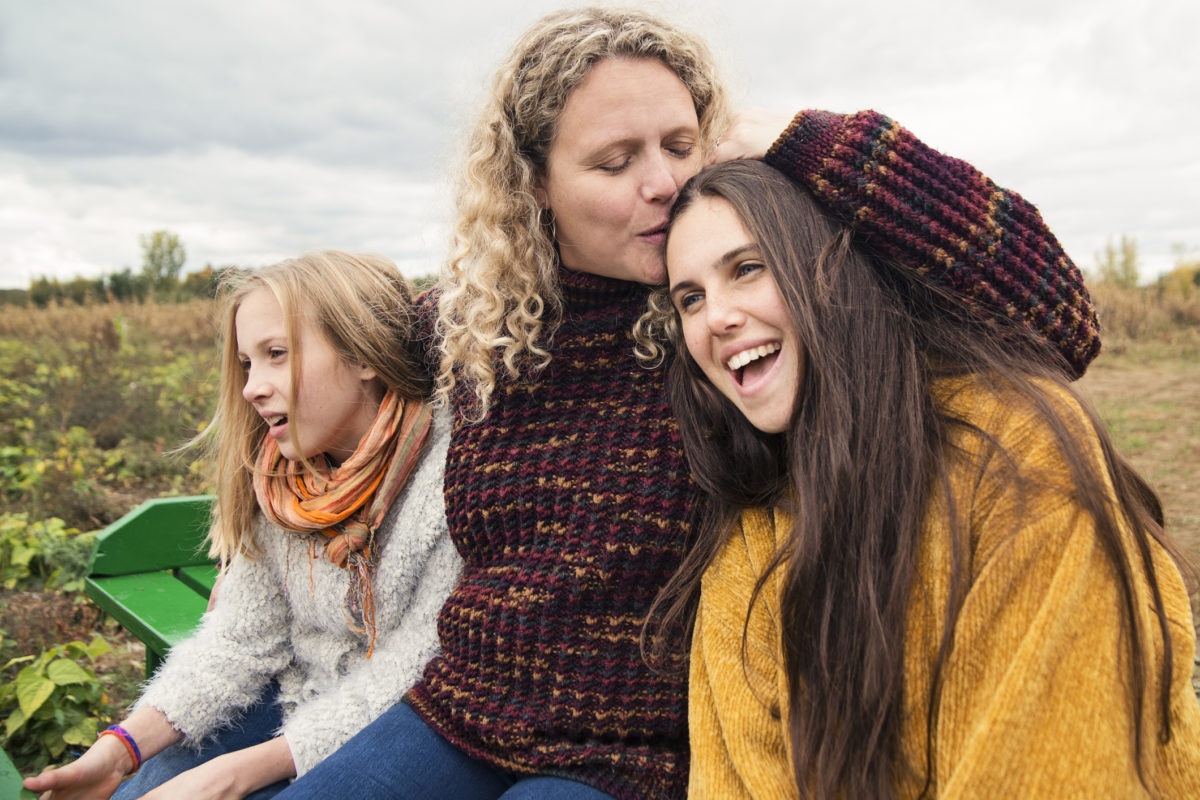 Smiling Mom Hugging and Kissing Her elder daughter and younger daughter.