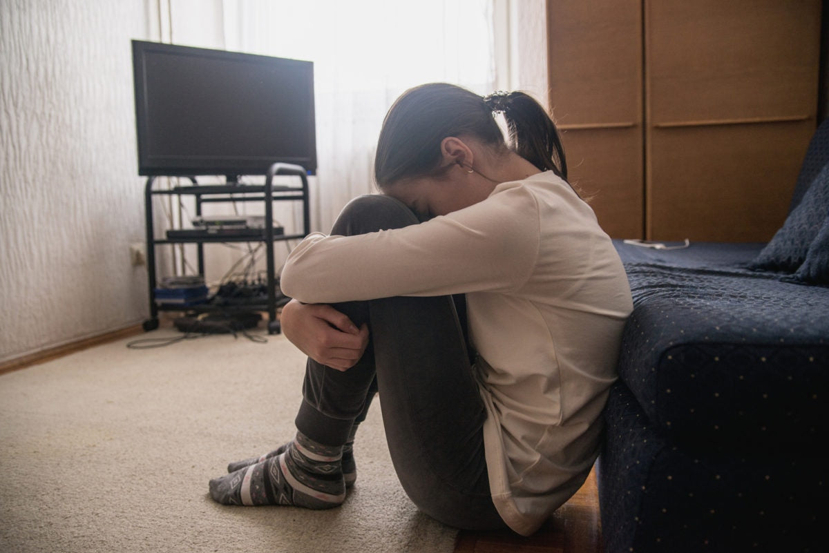 young girl upset sad and lonely holding head in hands crying huddled on