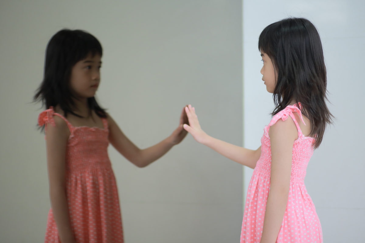 a girl touching the mirror and looking at her reflection