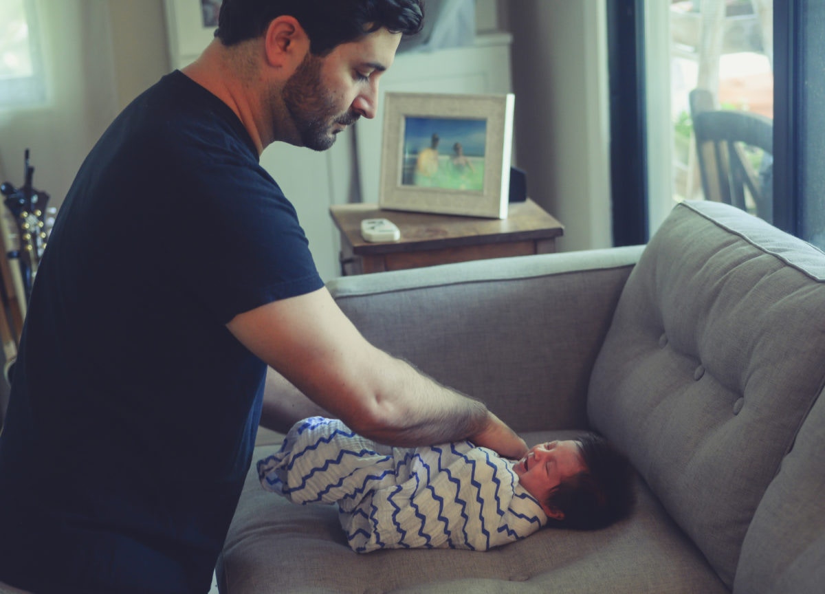 Father Swaddling His Newborn Baby on the couch