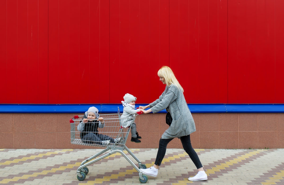 two kids in a shopping cart with a woman pushing the cart