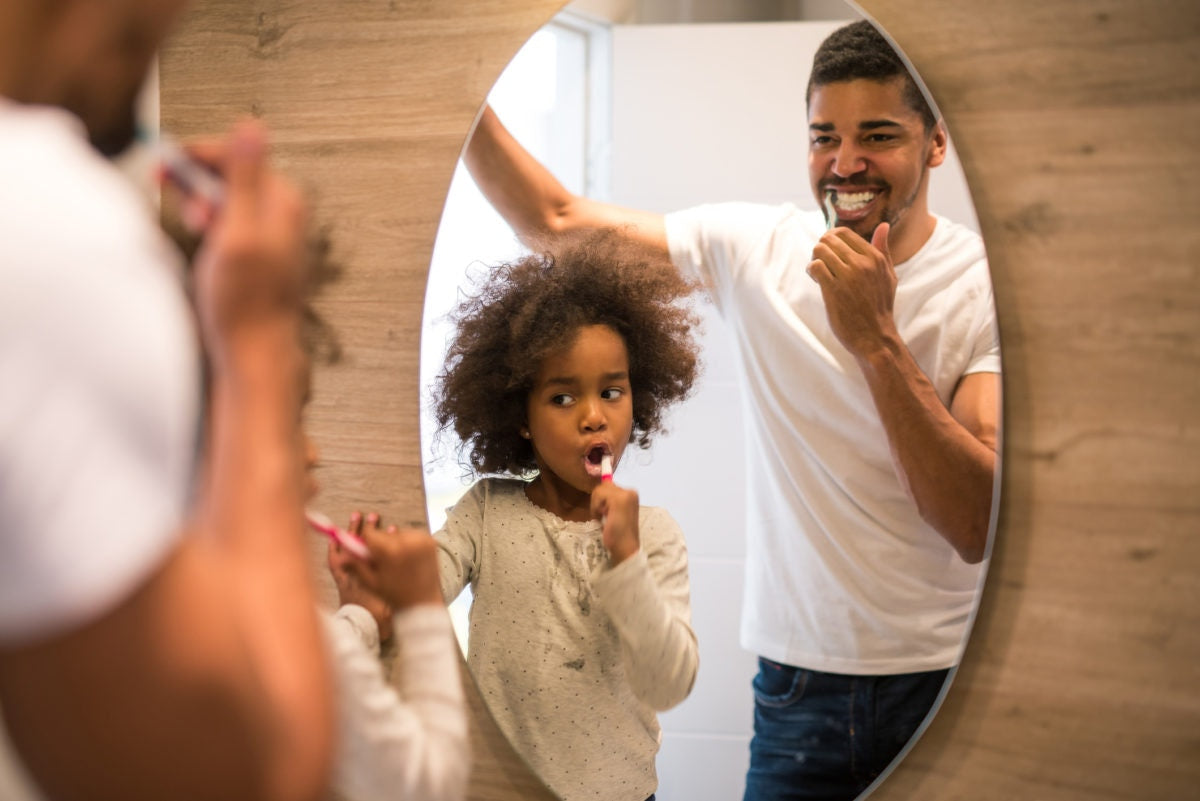 A Guy and child is brushing infront of mirror