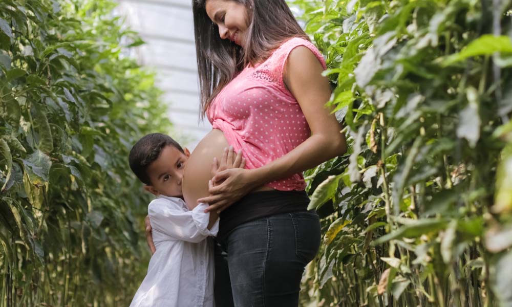 child kissing woman's pregnant belly